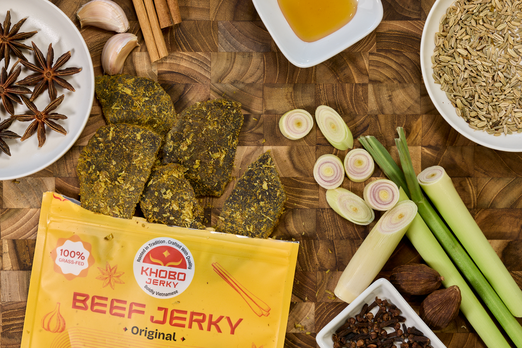 handcrafted grass fed vietnamese jerky displayed with fresh ingredients, lemongrass, whole spices like star anise, cinnamon and honey on a wooden board