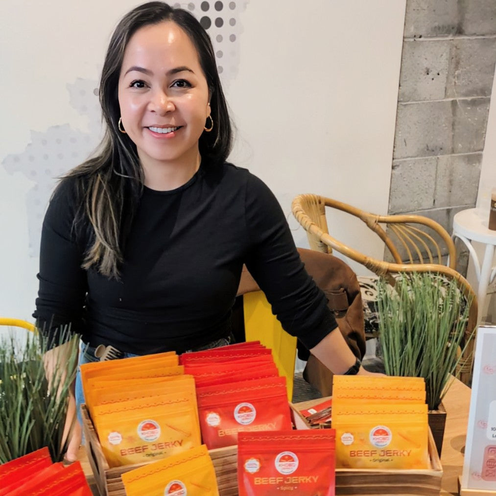 Asian minority woman standing behind her handcrafted Vietnamese beef jerky packages at a local pop up